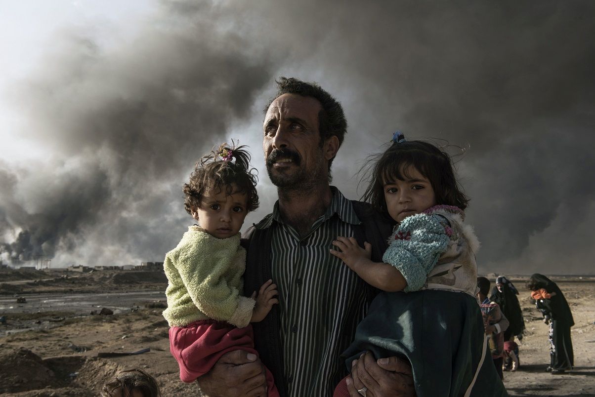 Iraq, Qarayya: A newly displaced man carries two children at the northern check point in Qayyarah, south of Mosul on October 31, 2016. Alessio Romenzi